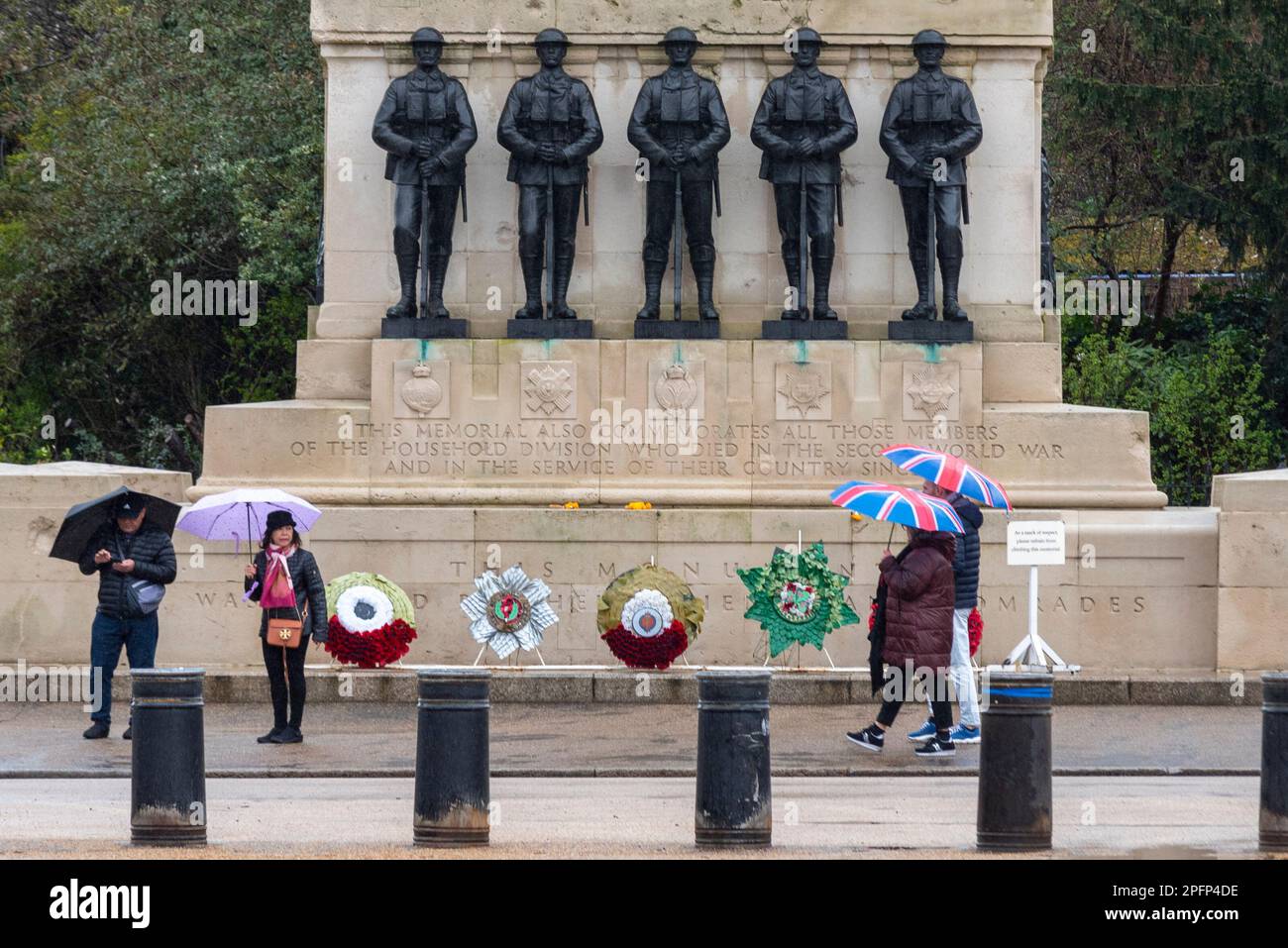 Westminster, London, UK. 18th Mar, 2023. The day has begun wet and overcast. People with Union Jack umbrellas passing Guards memorial. Stock Photo