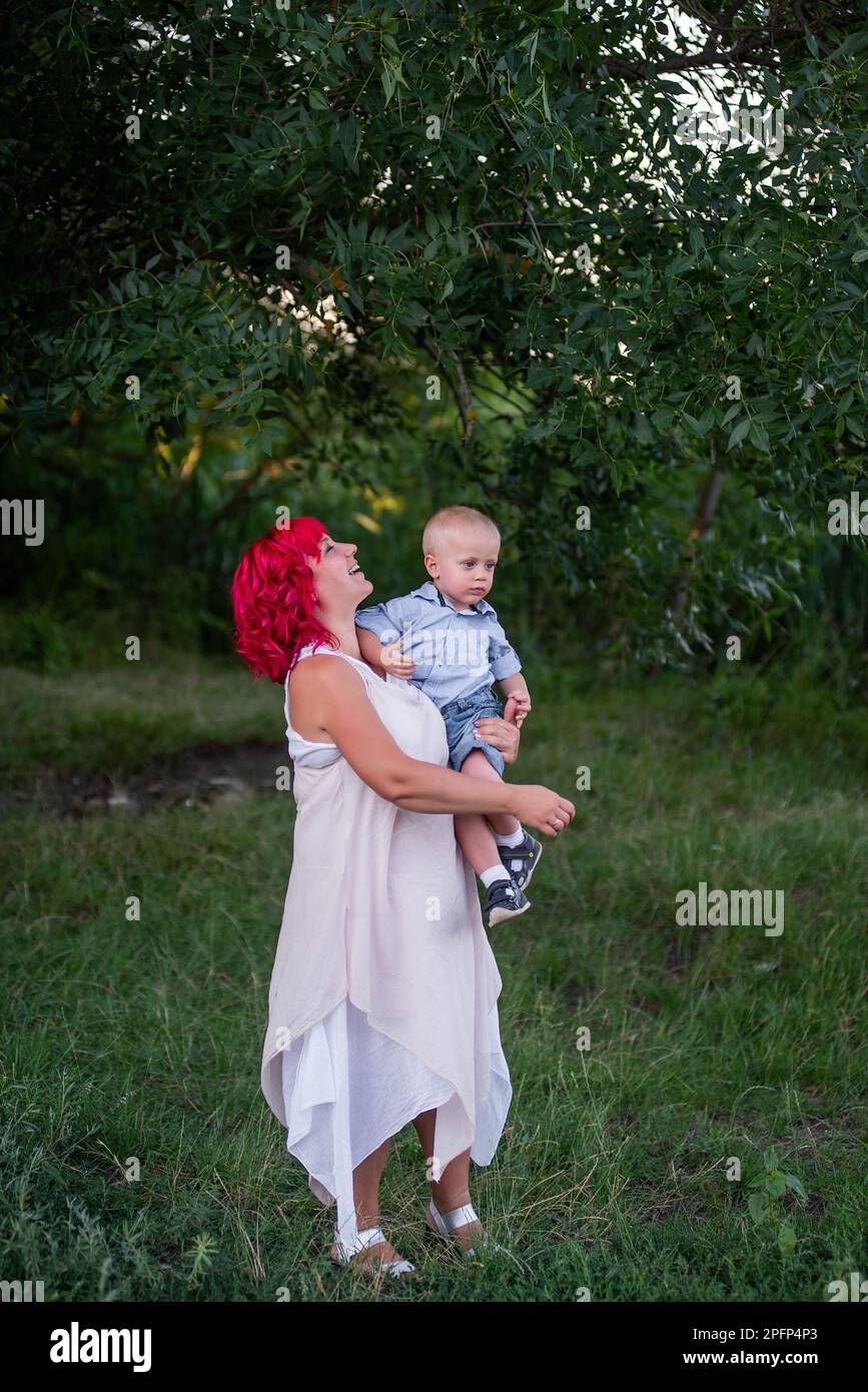 Portrait of bright, diversity, extraordinary mother and little son embrace in the forest. Woman has pink hair. Tender motherhood, happy childhood. Res Stock Photo