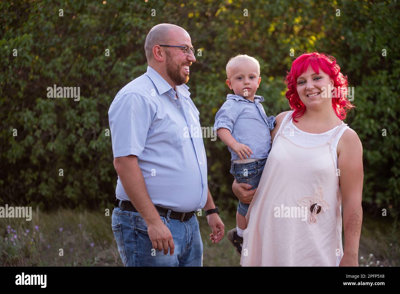 Bald father in glasses looks lovingly at wife with pink hair and son in blue shirt. Close-up portrait diversity family. Children Protection Day. Care Stock Photo