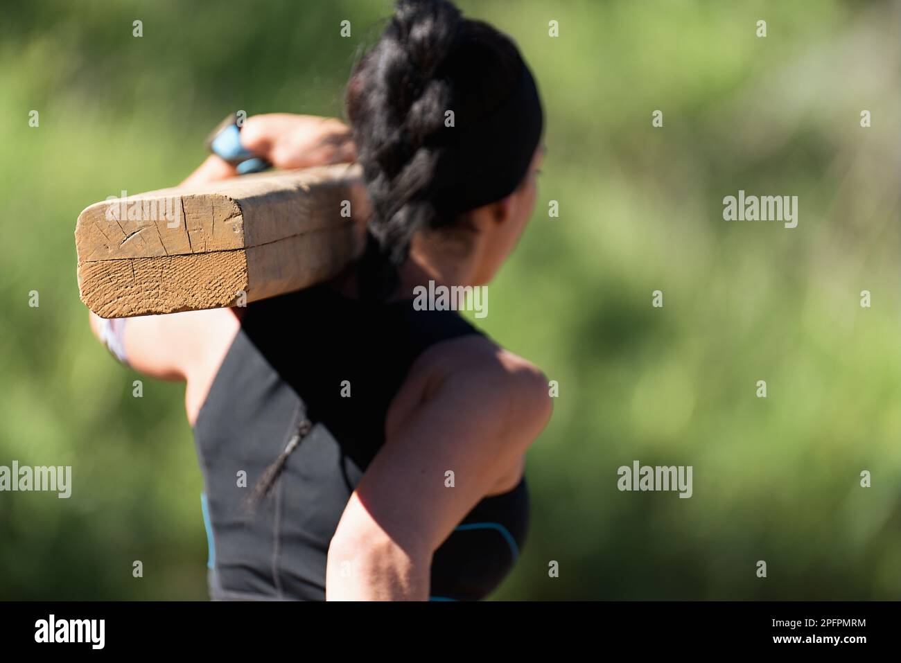 Woman carrying wooden log in a test of the race. Mud race runners, extreme obstacle race. Focused on the log Stock Photo