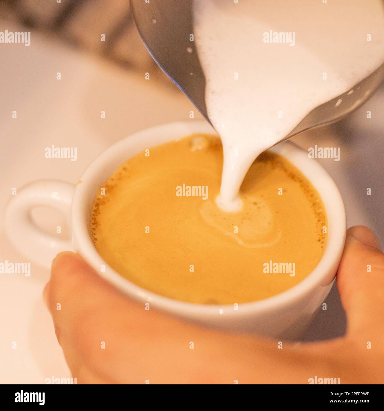 Caucasian bartender prepares coffee while pouring milk into white cup Stock Photo