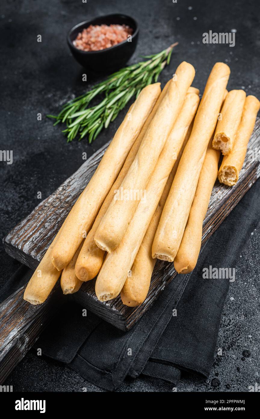 Italian grissini or salted bread sticks on wooden board. Black bakground. Top view. Stock Photo