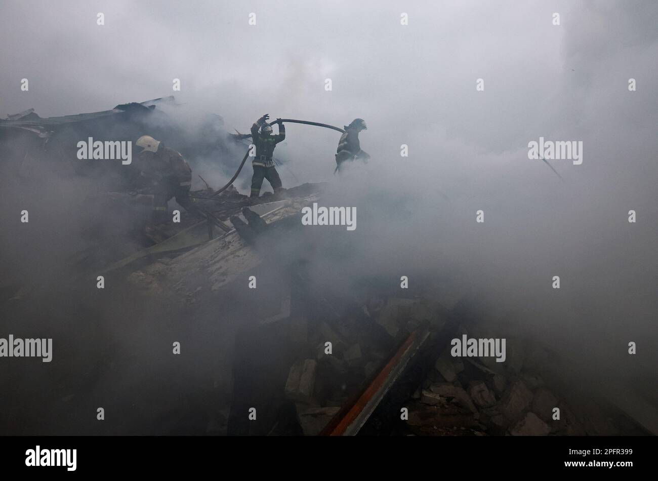 Firefighters work to extinguish fire amidst debris of a house destroyed by recent shelling in the course of Russia-Ukraine conflict in the city of Khartsyzk, in the Donetsk region, Russian-controlled Ukraine, March 18, 2023. REUTERS/Alexander Ermochenko Stock Photo
