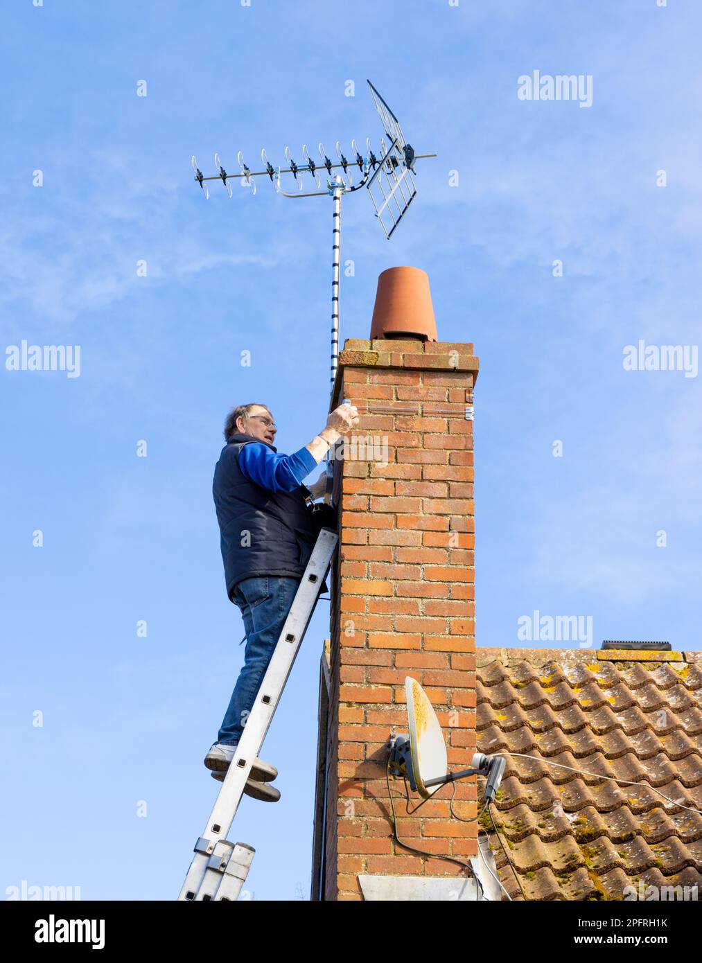 Man installing a new television aerial on a chimney stack. UK Stock
