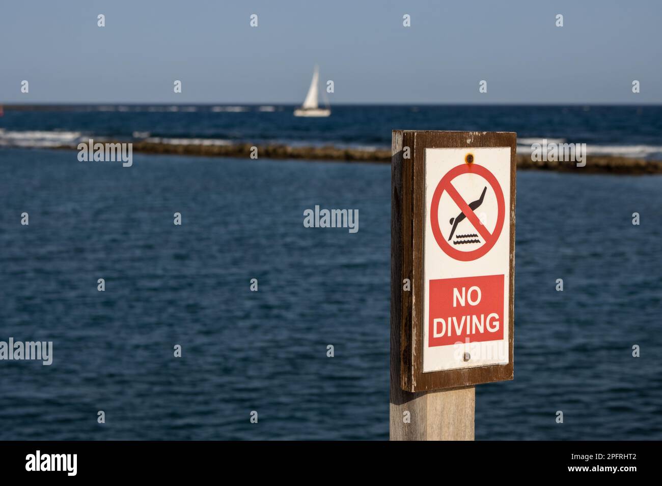 No diving advice on a wooden board. Atlantic ocean and a sailing boat in the blurry background. Blue sky. Fuerteventura, Canary Islands, Spain, Europe Stock Photo