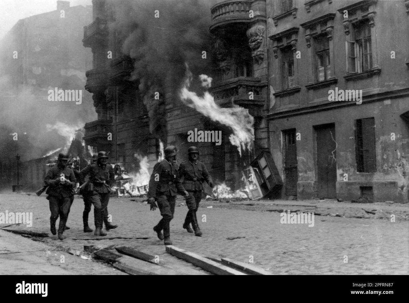 In January 1943 the nazis arrived to round up the Jews of the Warsaw Ghetto  The Jews, resolved to fight it out, took on the SS with homemade and primitive weapons. The defenders were executed or deported and the Ghetto area was systematically demolished. This event is known as The Ghetto Uprising. This image shows a group of German soldiers walking down burning Nowolpie Street. This image is from the German photographic record of the event, known as the Stroop report. Stock Photo