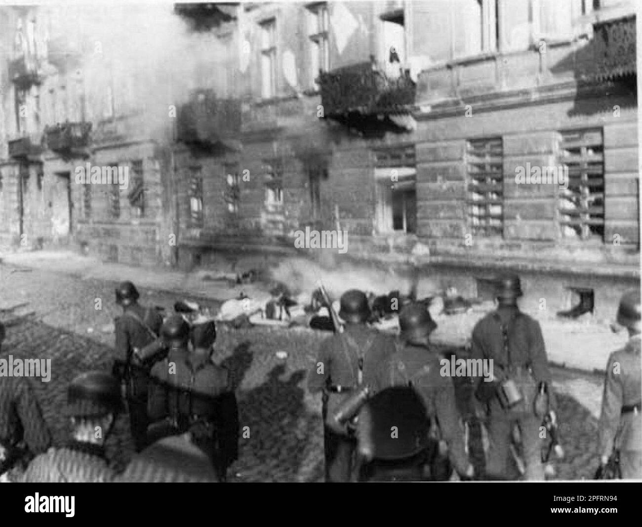 In January 1943 the nazis arrived to round up the Jews of the Warsaw Ghetto  The Jews, resolved to fight it out, took on the SS with homemade and primitive weapons. The defenders were executed or deported and the Ghetto area was systematically demolished. This event is known as The Ghetto Uprising. This image shows SS troops standing near the bodies of Jews who committed suicide by jumping from a fourth story window rather than be captured. This image is from the German photographic record of the event, known as the Stroop report. Stock Photo