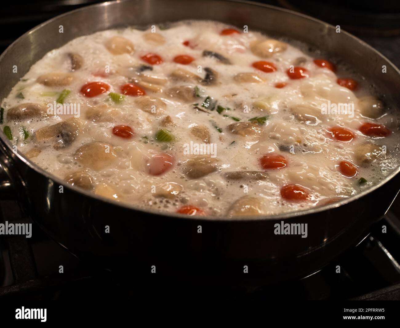 Delicious Thai coconut soup with tomatoes in a silvery pot. Stock Photo