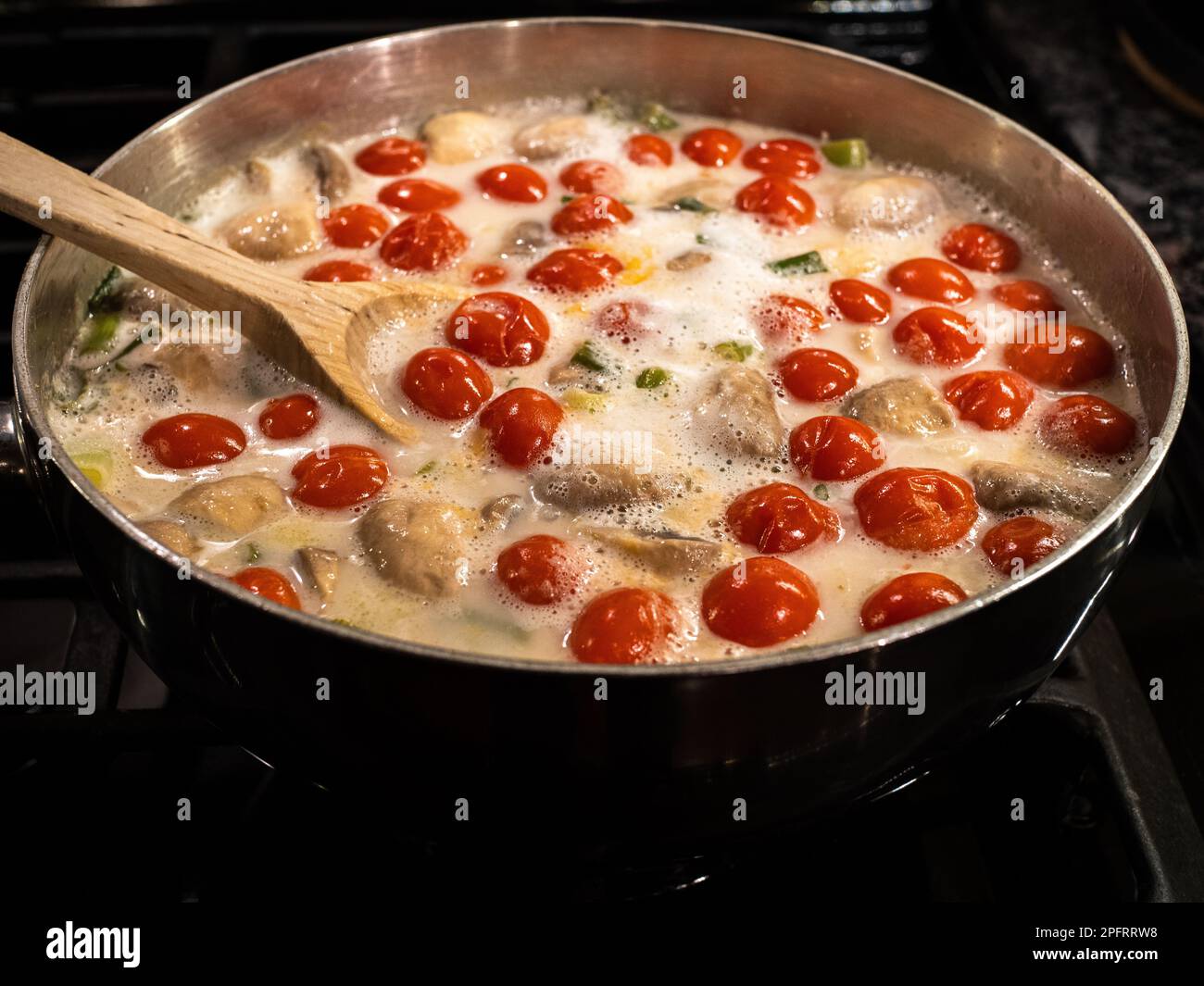 Delicious Thai coconut soup with tomatoes in a silvery pot with wooden utensil. Stock Photo
