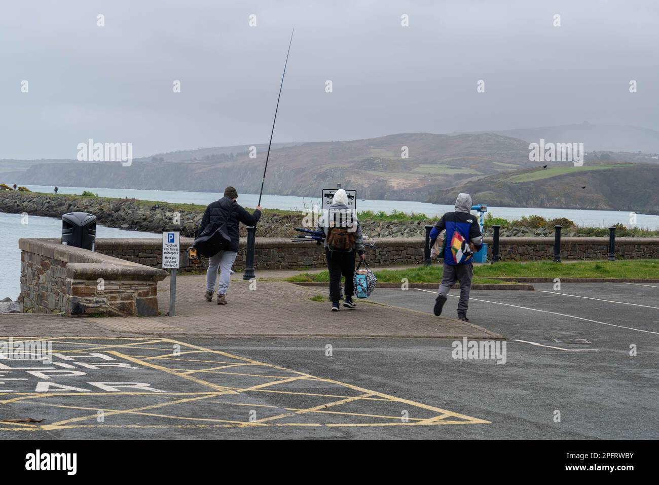 Local fisherman walking along sea wall with fishing gear at Fishgaurd Pembrokeshire Stock Photo