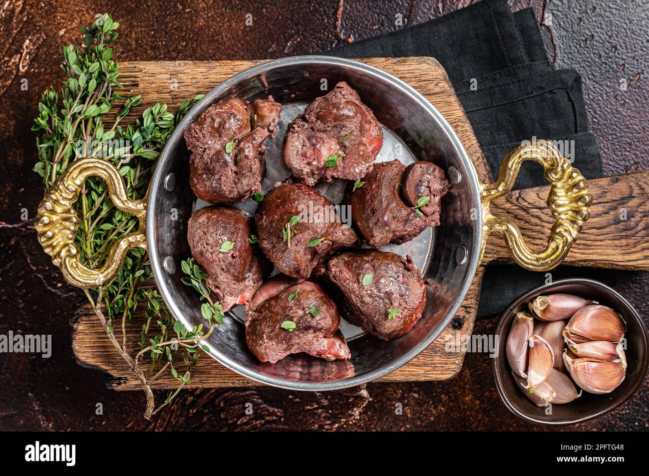 Roasted beef kidney offal meat in skillet with herbs Dark background