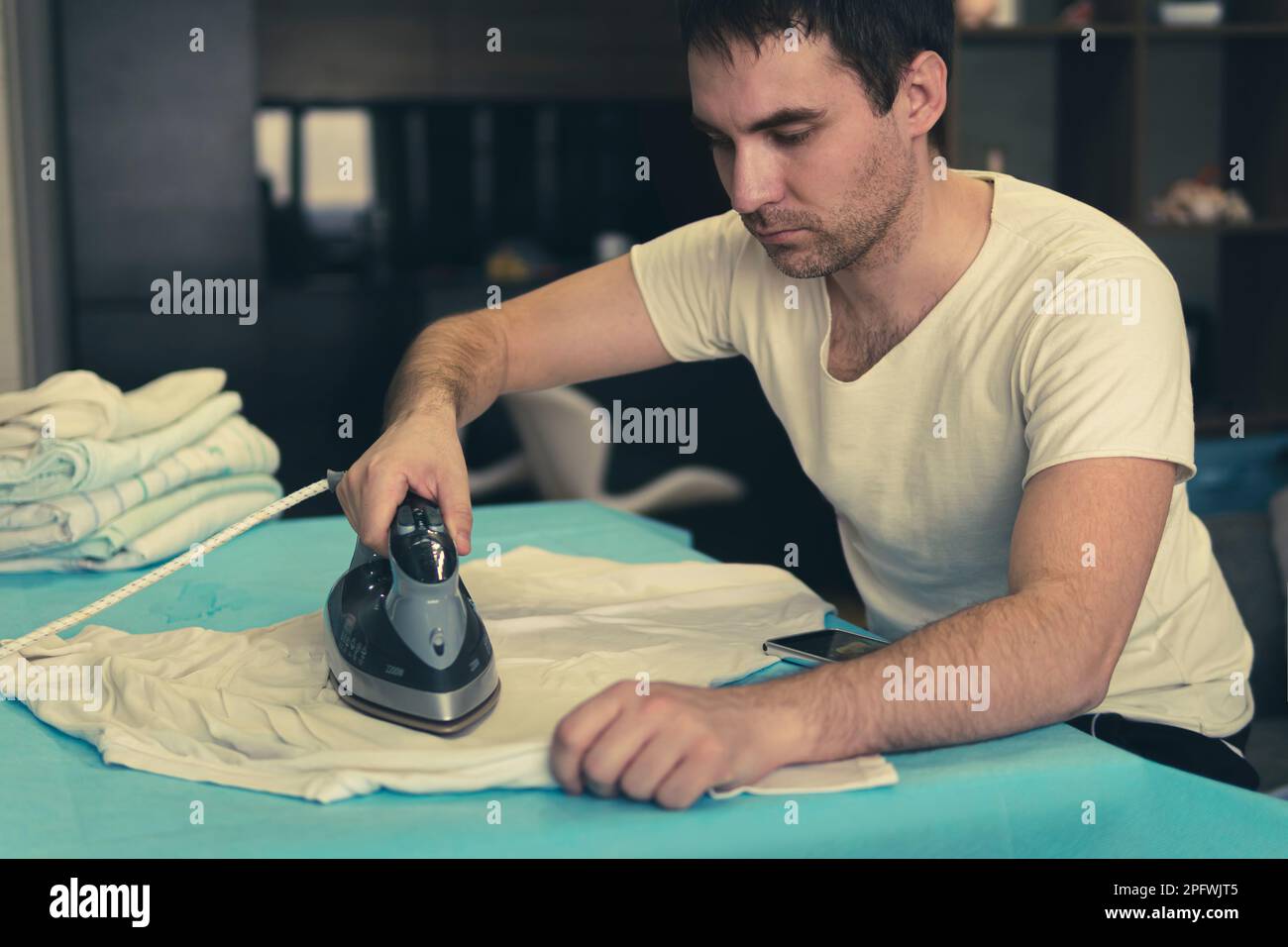 A young man irons his clean clothes after washing at home against the