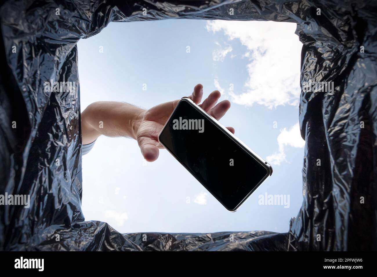 a man throws a non-working smartphone into a trash can. Bottom view from the trash can. The problem of recycling and pollution of the planet with garb Stock Photo