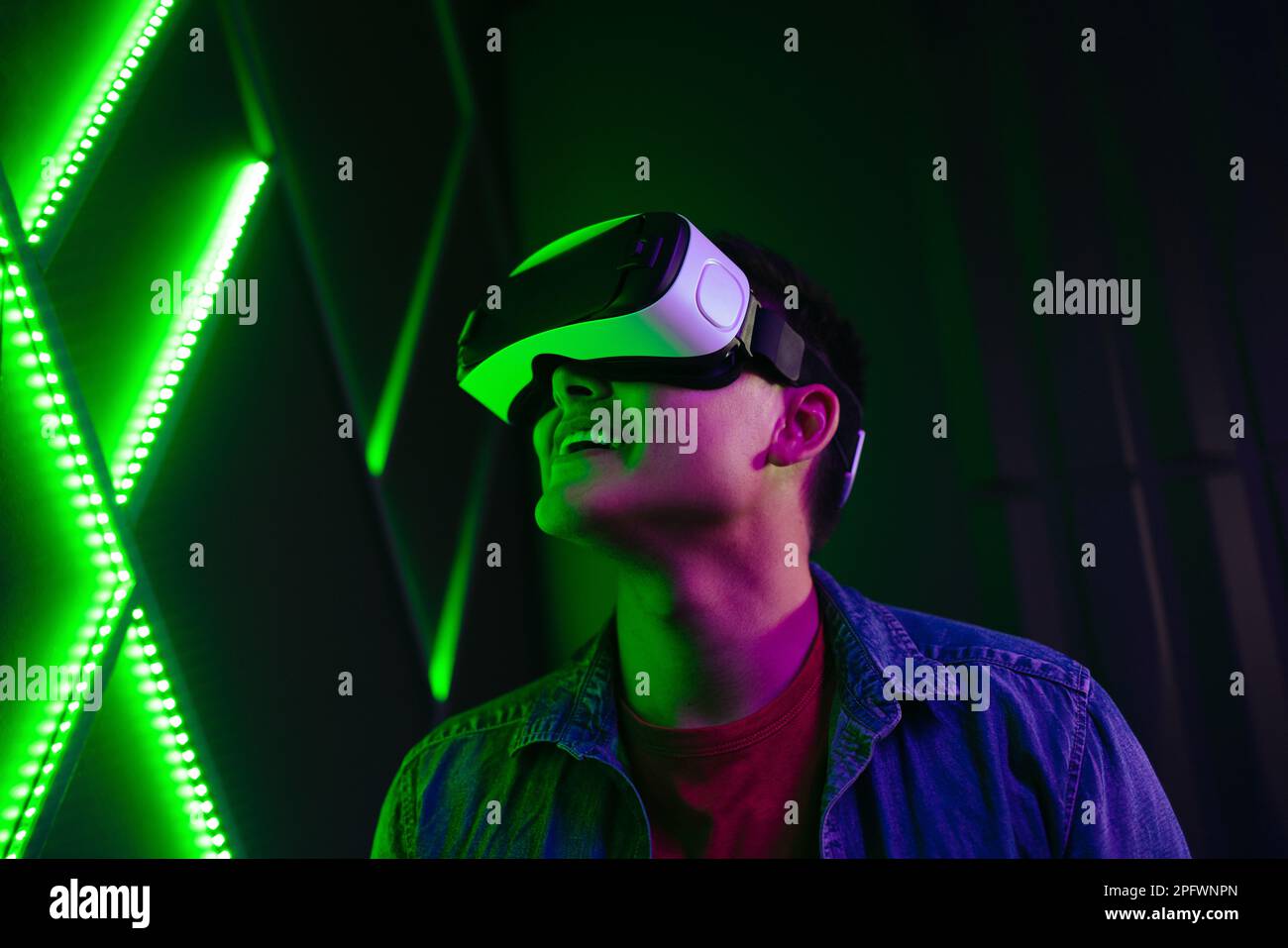 Man watching objects in virtual reality with a smile on his face. Tech-savvy young man experiencing an exciting game using VR goggles, immersing himse Stock Photo