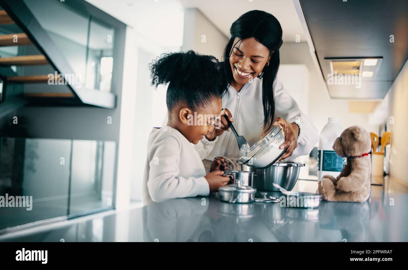 Woman teaching her daughter how to mix flour for baking. Happy mom making a cake with her daughter in the kitchen. Mother passing a family recipe to h Stock Photo