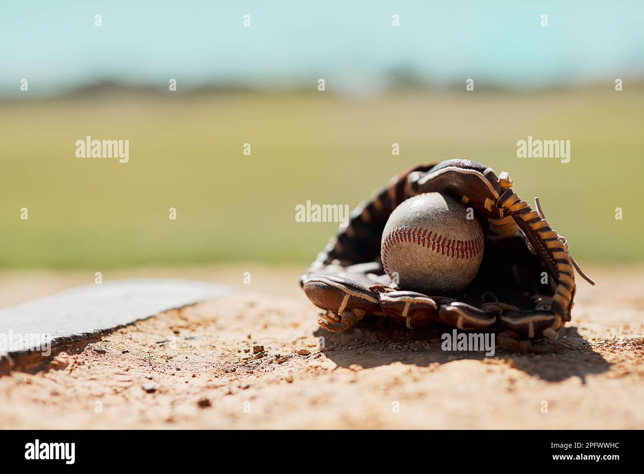 Step up to the plate. a baseball mitt and ball lying on the pitch during the day. Stock Photo