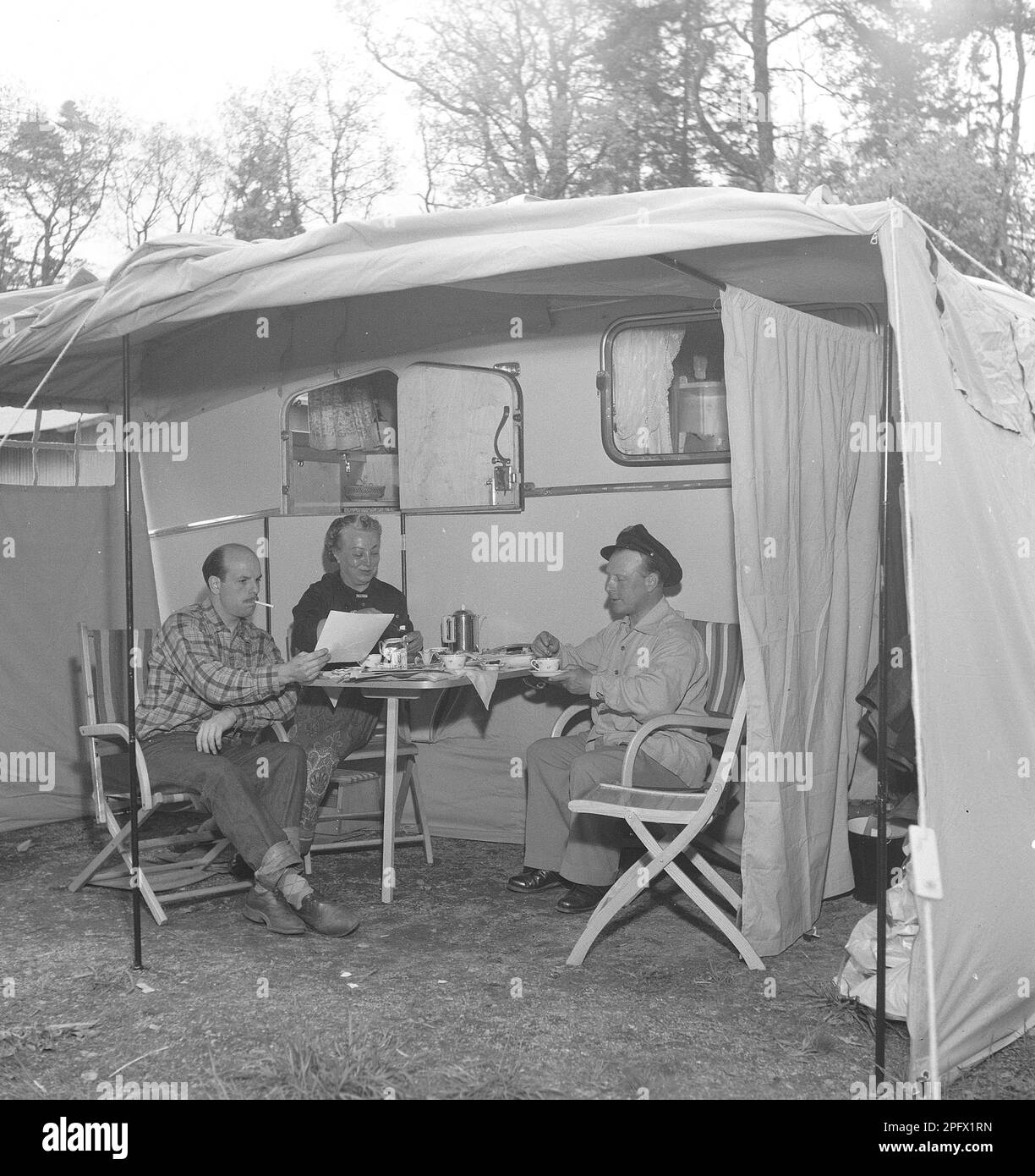 1950s camping. Three people are sitting by their caravan enjoying a cup of coffee. The use of caravans to spend the summer holiday was fairly new at this time.  Sweden July 1953. Kristoffersson ref BP30-9 Stock Photo