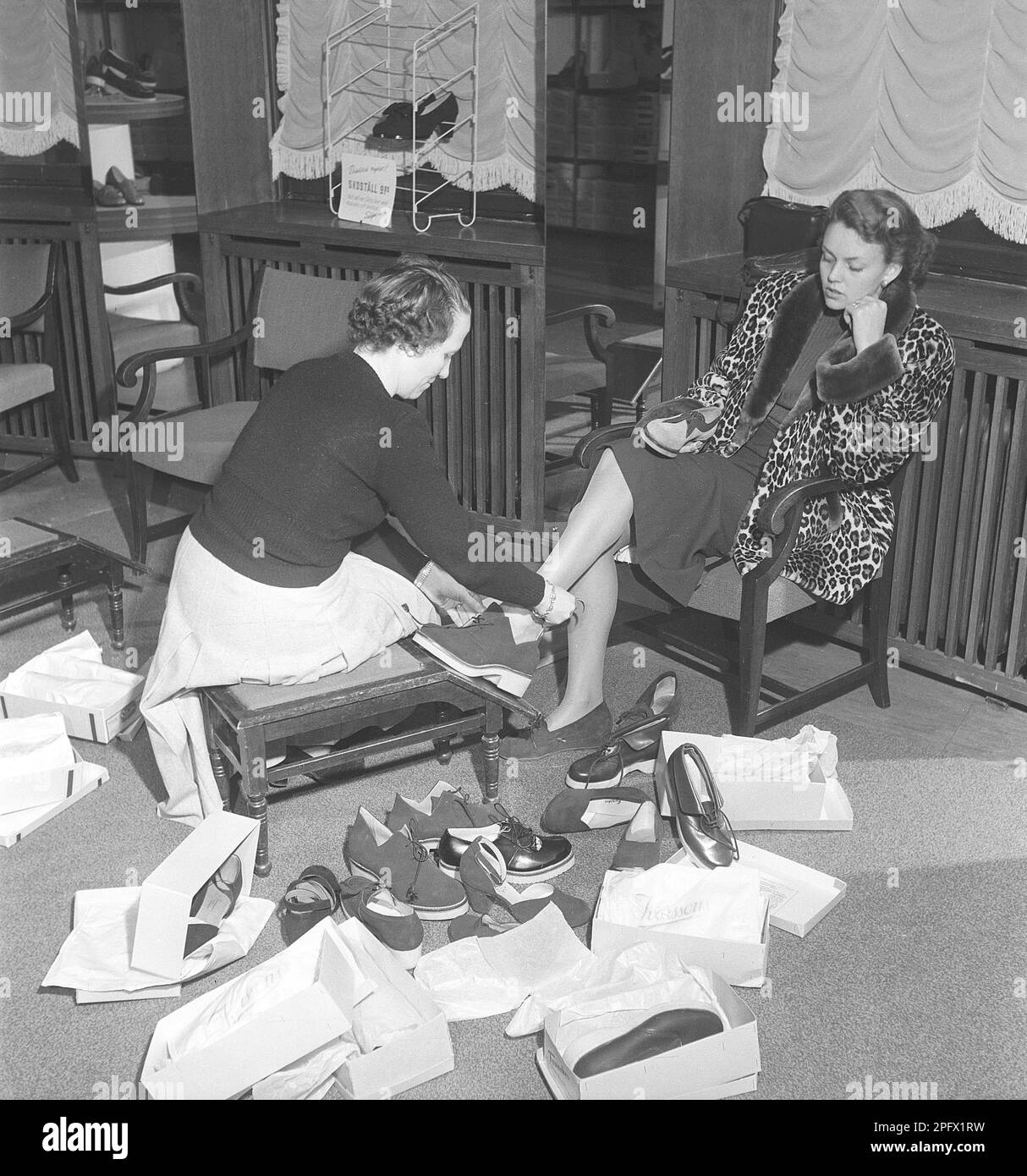 A young woman is well taken care of by a clerk in a shoe store. The dispatcher tries different shoes on the lady's feet. She has tried several different pairs of summer shoes and, judging by the picture, she has not yet found a pair that she thinks fits. Sweden 1949 Kristoffersson ref AU10-10 Stock Photo