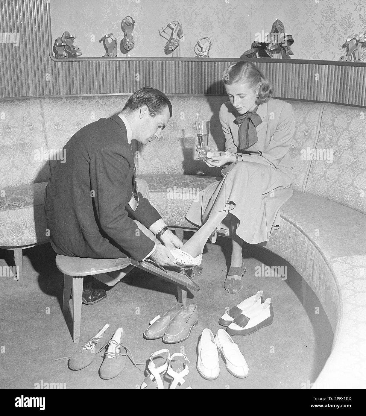 A young woman is well taken care of by a clerk in a shoe store. The dispatcher tries different shoes on the lady's feet. She has tried several different pairs of summer shoes and, judging by the picture, she has not yet found a pair that she thinks fits. Sweden 1949 Kristoffersson ref AS15-1 Stock Photo