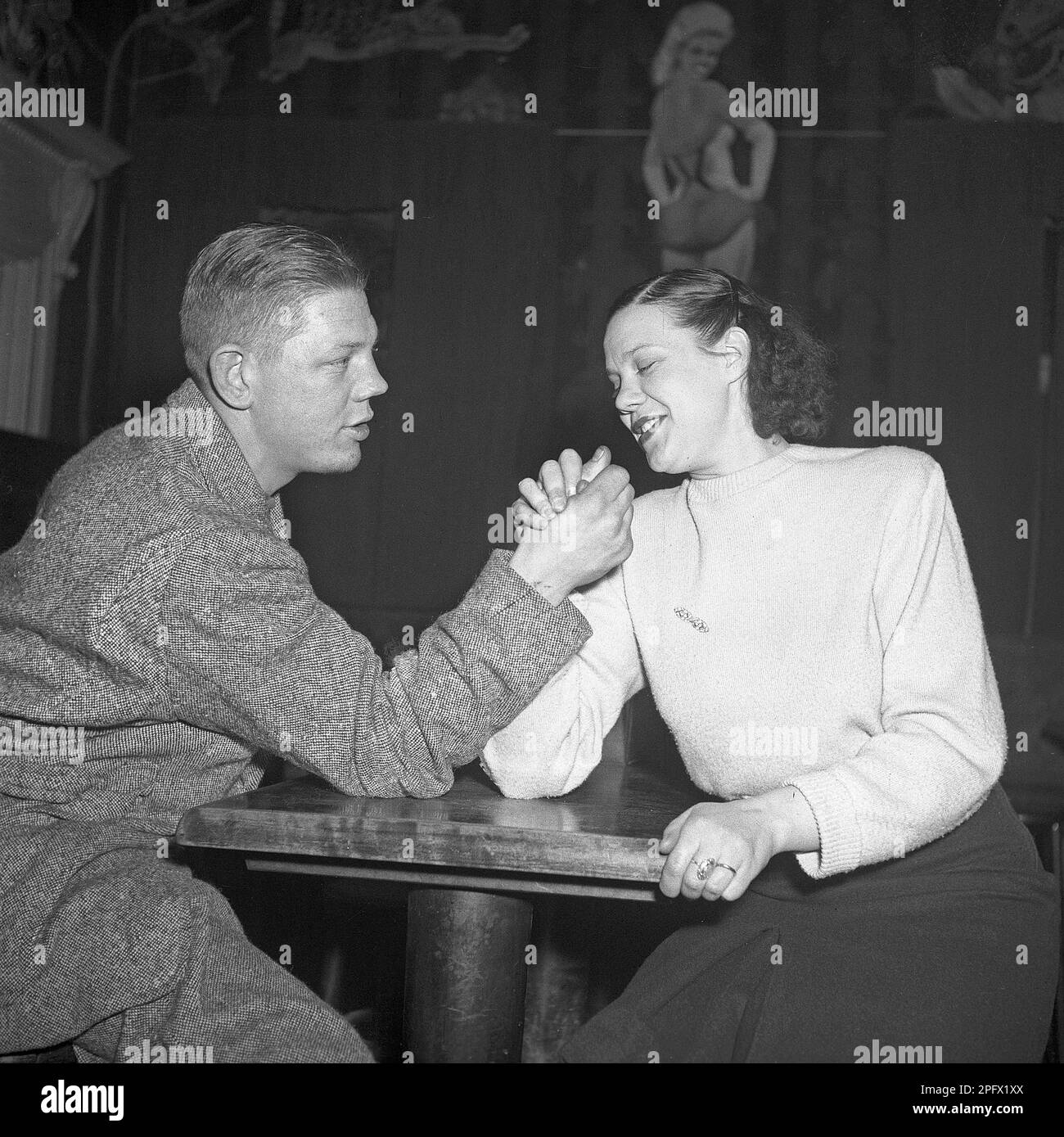 Who's the strongest? A young couple try their strenght at armwrestling in a restaurant. Sweden 1948 Kristoffersson Ref AG46-1 Stock Photo