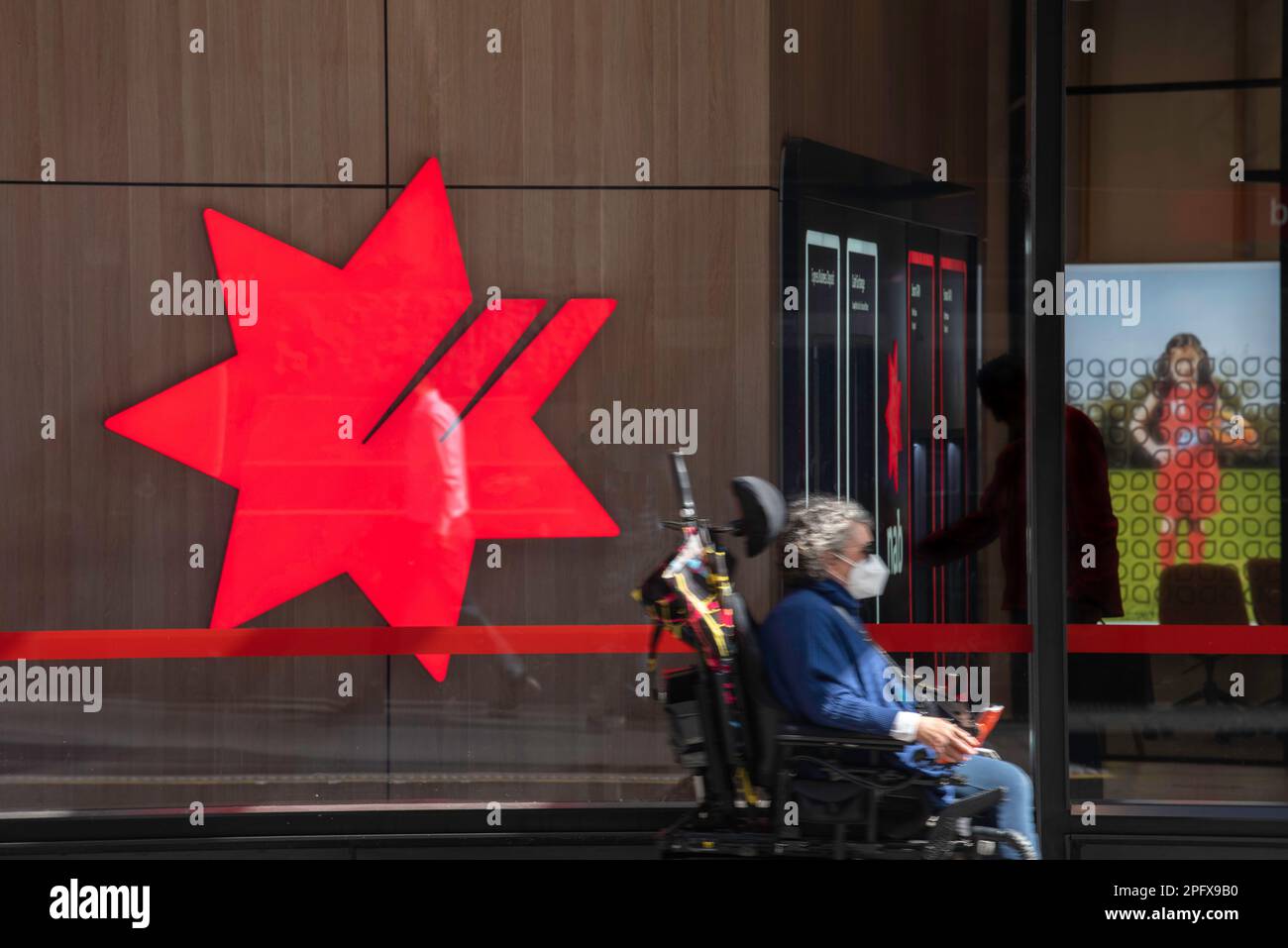 A woman in a motorised wheelchair moves past a National Australia Bank (Nab bank) logo sign on the interior of a building in Sydney, NSW, Australia Stock Photo