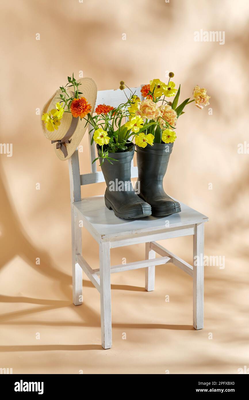 flowers in rubber boots and hat on vintage chair Stock Photo - Alamy