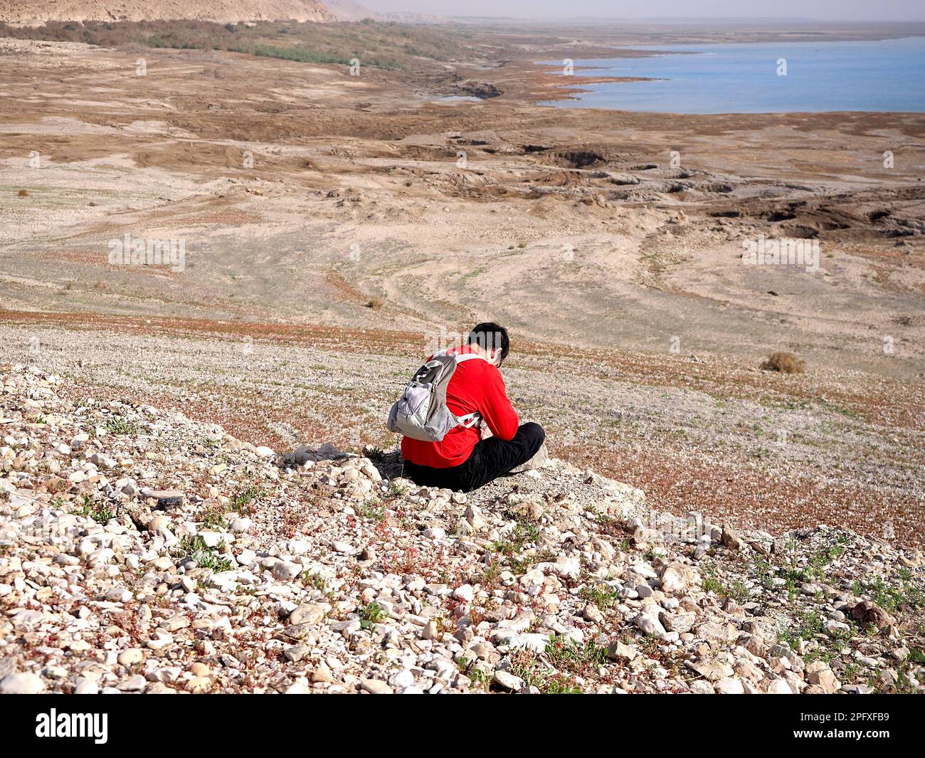 A man with a backpack sits on the coast of the Dead Sea. Stock Photo