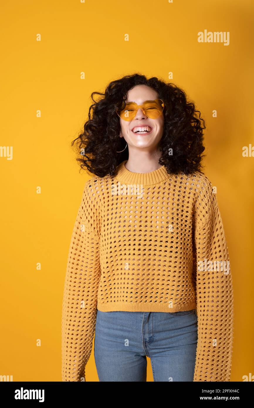 laughing girl with curly black hair and fashion glasses on yellow background Stock Photo