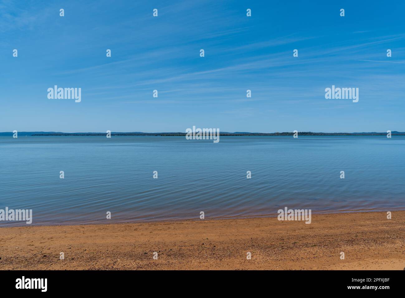 View from Redland Bay across smooth, calm water, to southern Moreton Bay islands on the horizon, under a beautiful blue sky with cirrostratus clouds Stock Photo