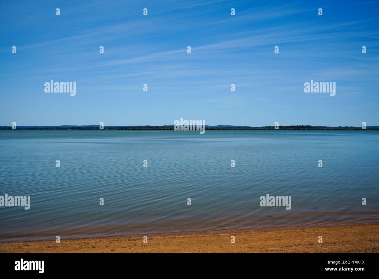 View from Redland Bay across smooth, calm water, to southern Moreton Bay islands on the horizon, under a beautiful blue sky with cirrostratus clouds Stock Photo