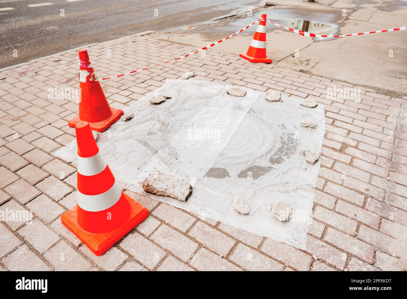 Plastic red cones warn pedestrians about repair of the sidewalk and sewerage hatchway. Moscow, Russia. Stock Photo