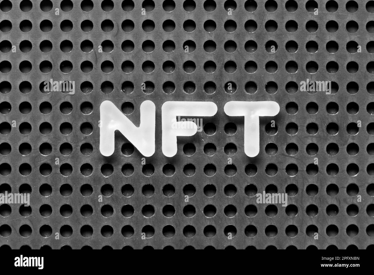 White alphabet letter in word NFT (Abbreviation of Non-fungible token) on black pegboard background Stock Photo