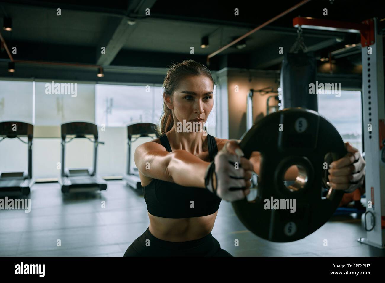 Sporty woman exercising with weight plate in the gym. Stock Photo