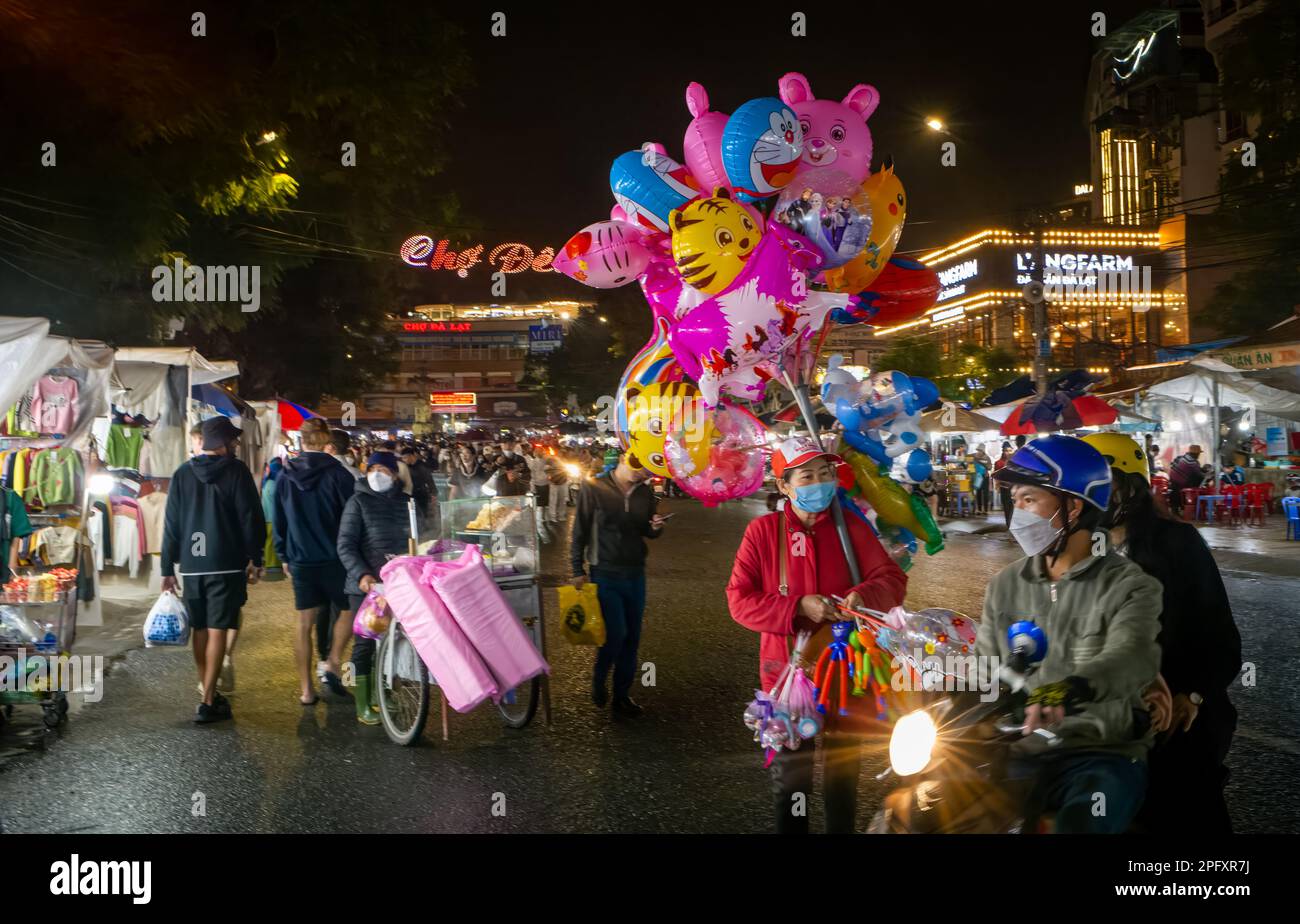 A balloon seller walks through the crowded and bustling night market in Dalat, Vietnam. Stock Photo