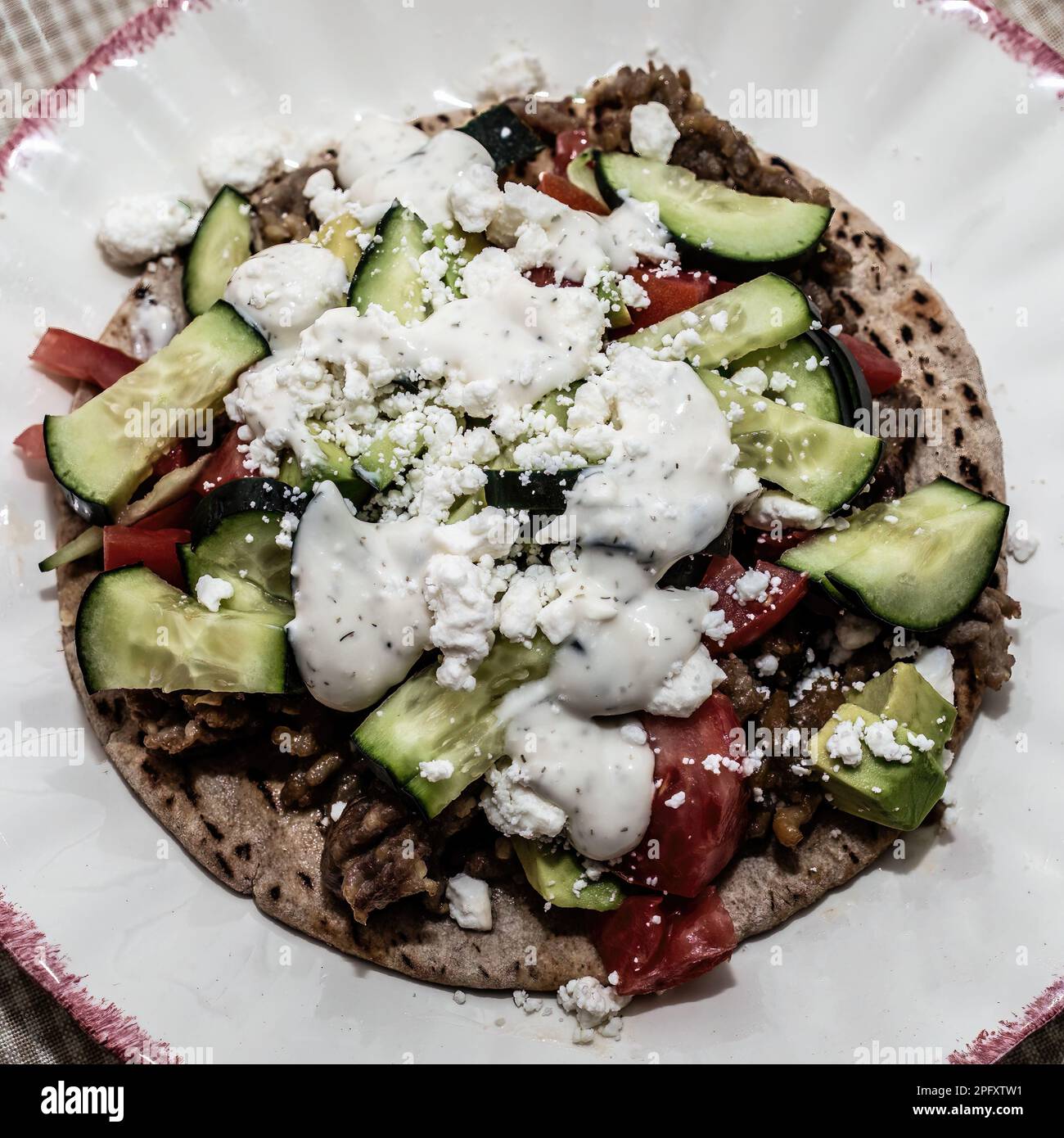 Greek sausage pita pizza with garlic, tomato, avocado, cucumber, feta