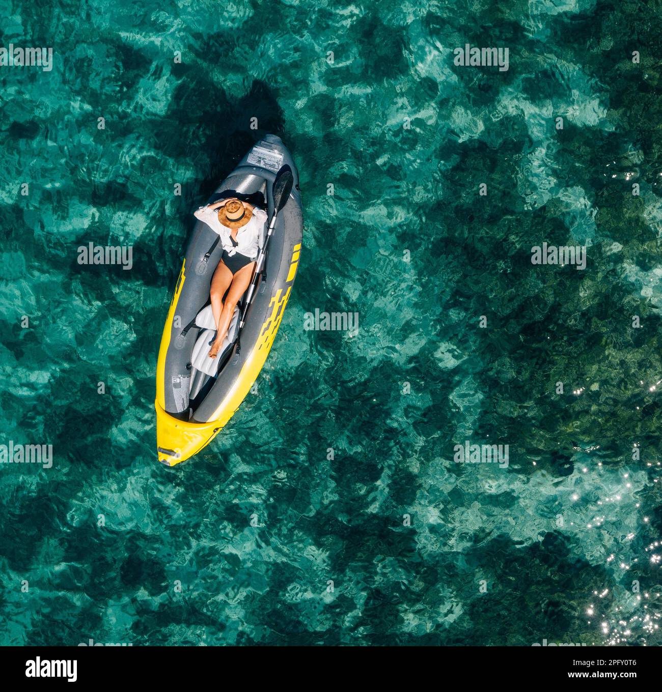 A lonely female in a straw hat smiling, relaxing lying floating in a kayak on the turquoise
