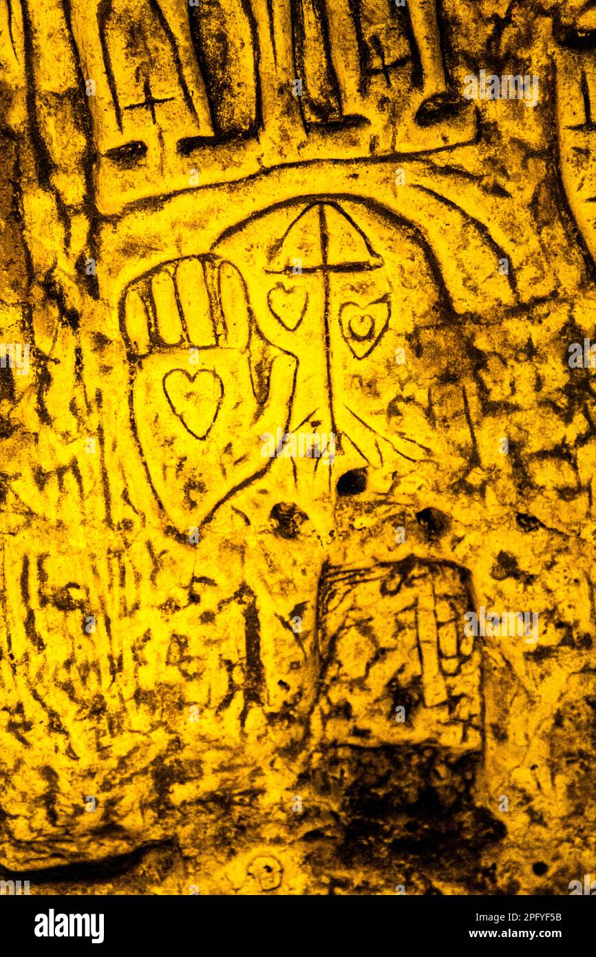 Royston Cave in Herfordshire U.K. still puzzles historians today. The cave is decorated with a large number of low-relief wall sculptures. They are mainly Christian motifs in the medieval style. The lower part of the Cave is covered with names cut by visitors and a palm with an engraved heart. Royston Cave in Katherine's Yard, Melbourn Street, Royston, England Stock Photo