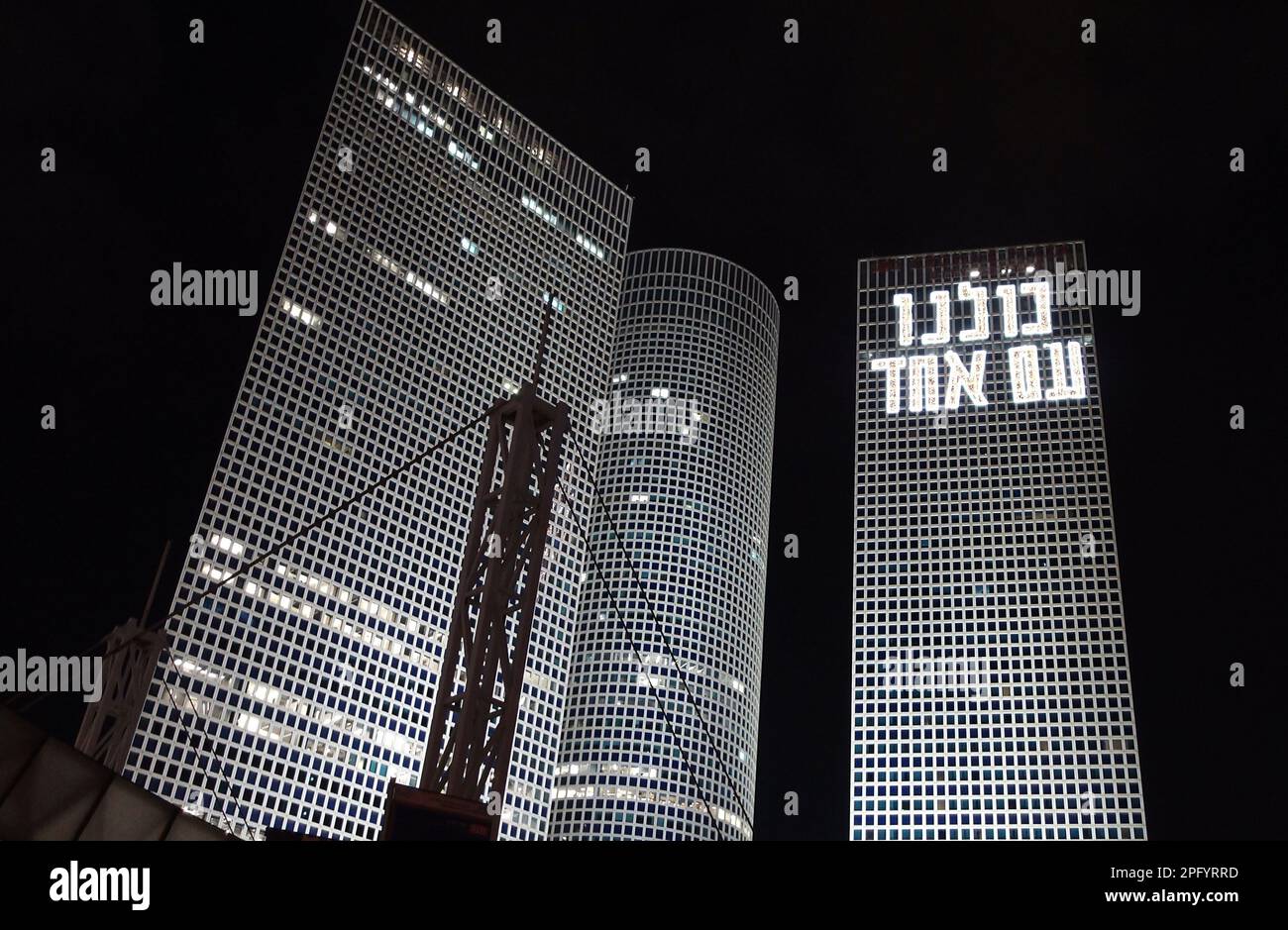 TEL AVIV, ISRAEL - MARCH 18: An illuminated sign in Hebrew in the skyscraper towers of Azrieli Center reads 'We are all one nation' as anti government protesters gather near the buildings during a demonstration for the 11th consecutive week against Israel's hard-right government judicial system plan that aims to weaken the country's Supreme Court on March 18, 2023 in Tel Aviv, Israel. Credit: Eddie Gerald/Alamy Live News Stock Photo