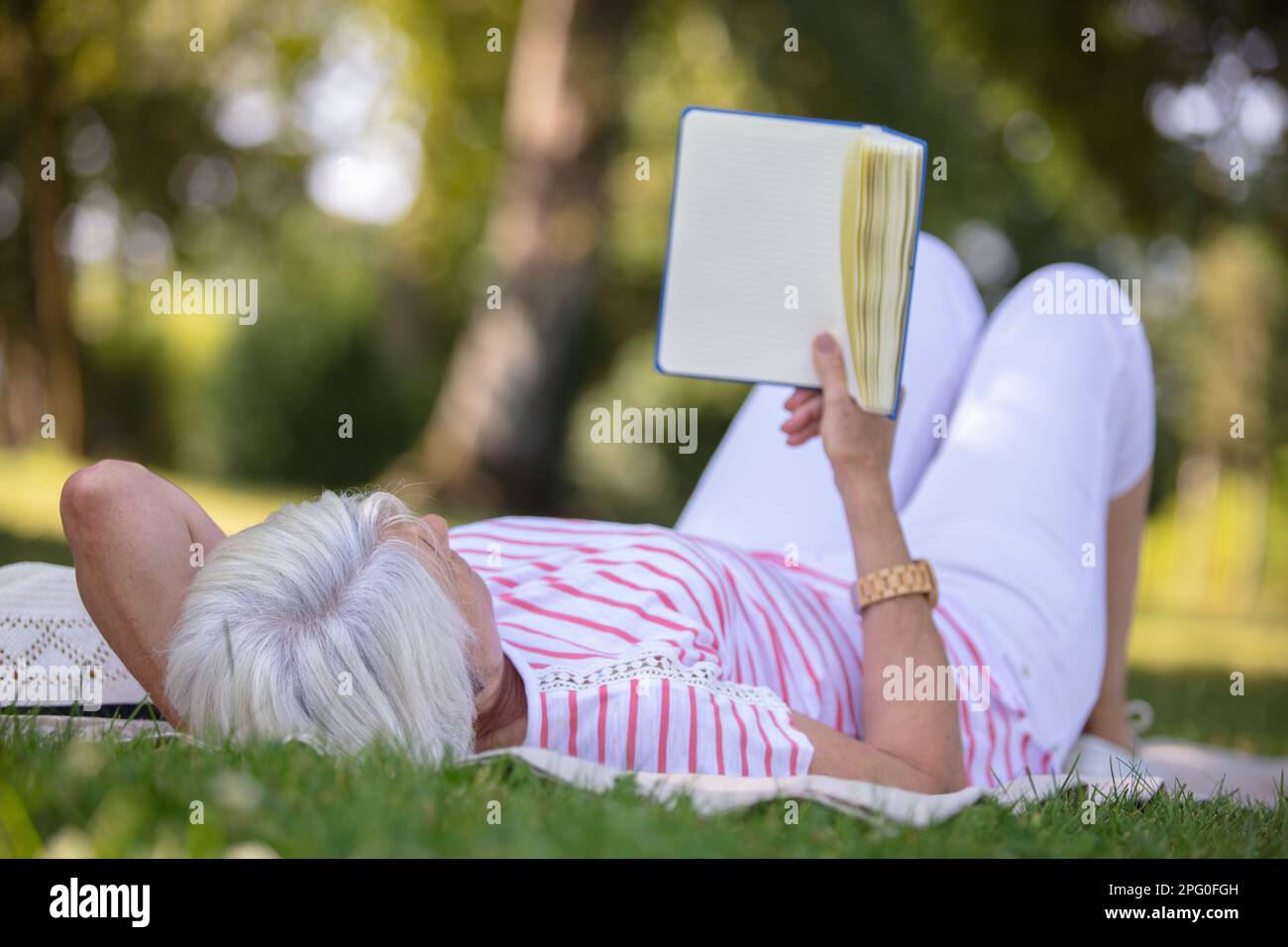 senior woman reading book laid on the grass Stock Photo - Alamy