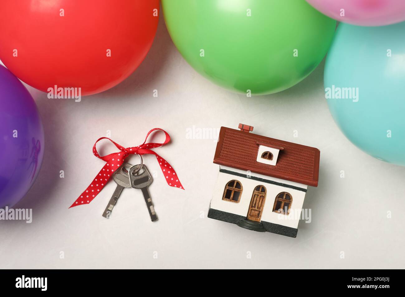 Wooden house model, keys with bow and balloons on white table, flat lay