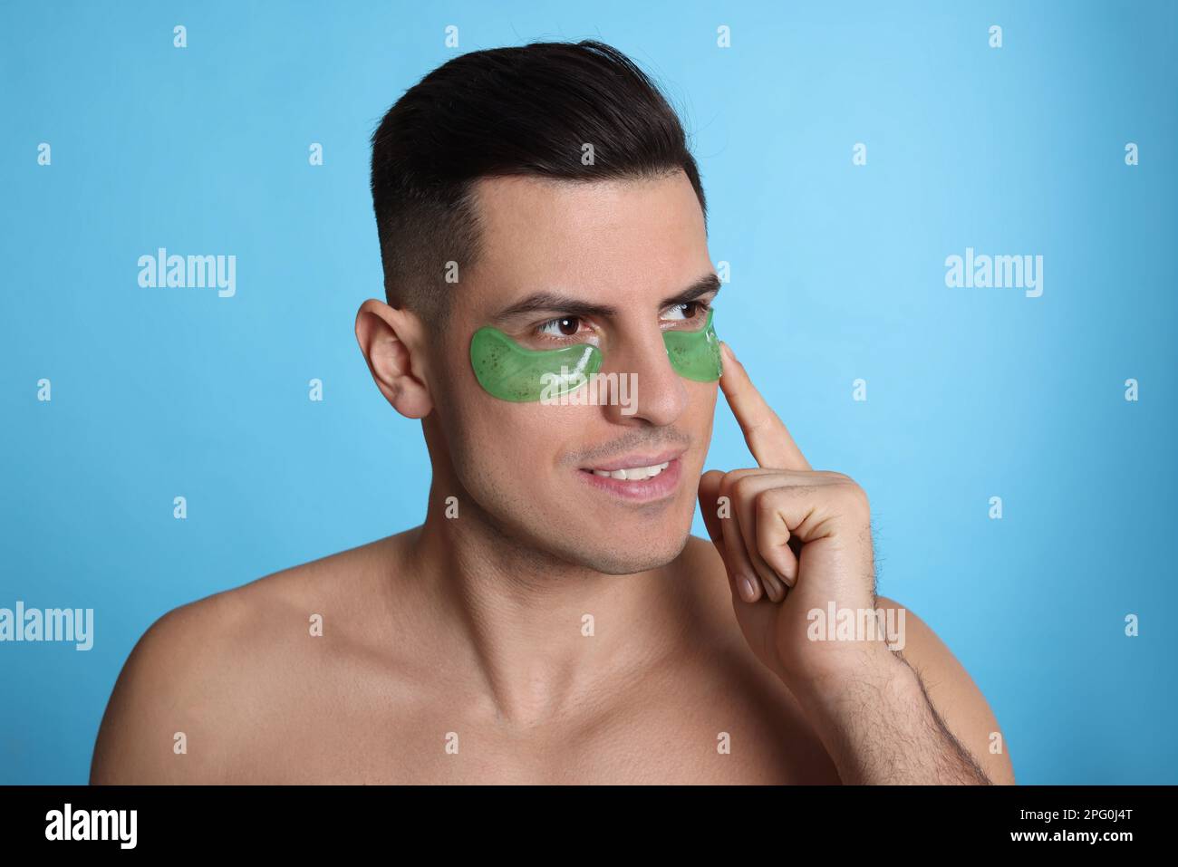 Man applying green under eye patch on light blue background Stock Photo