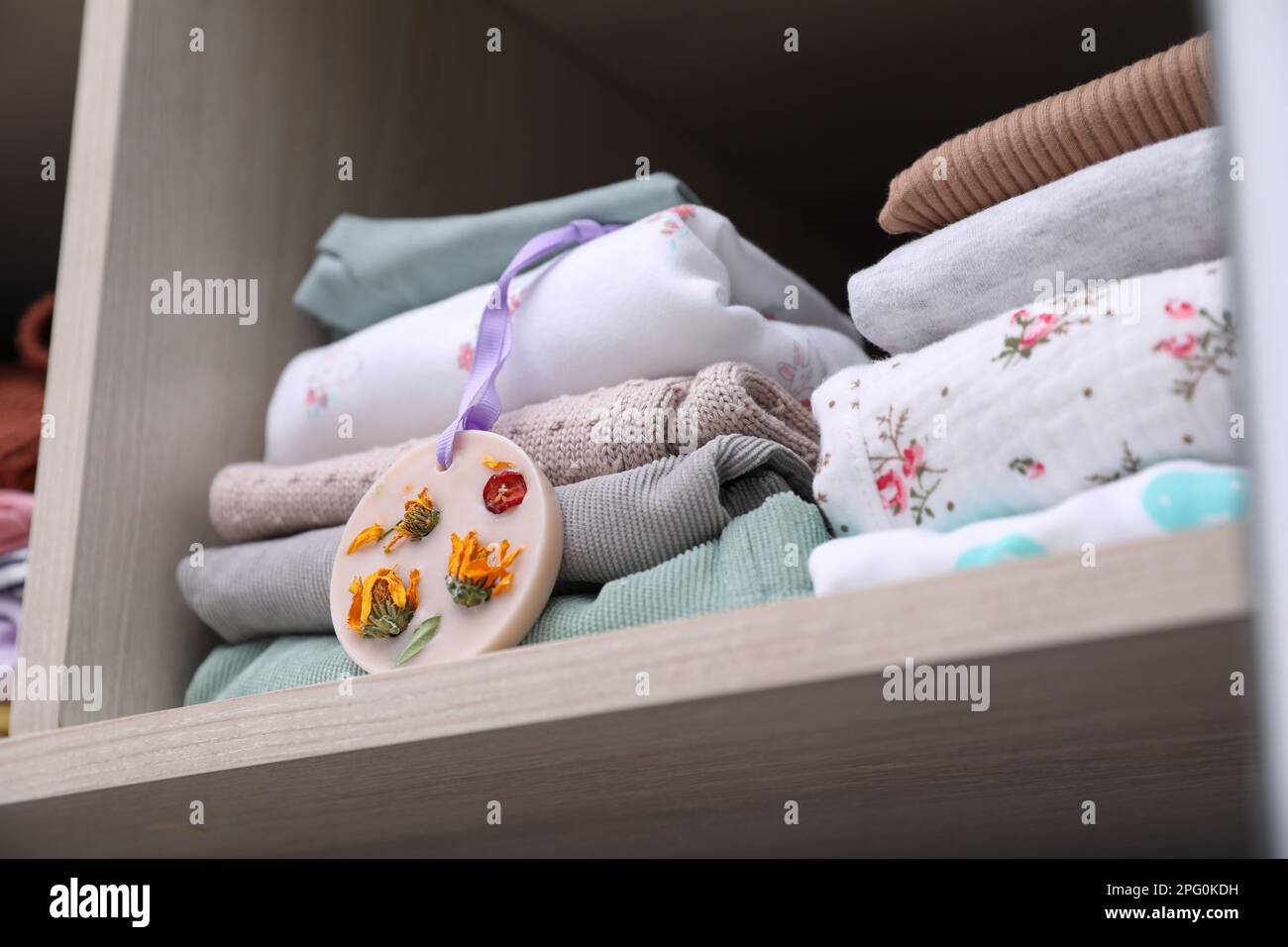 Beautiful scented wax sachet near stack of clothes on shelf in wardrobe