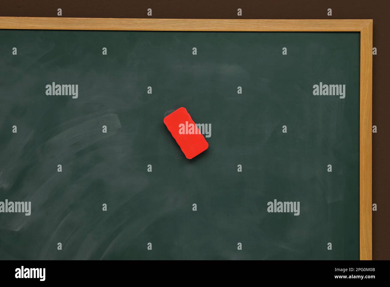 Dirty green chalkboard with duster hanging on brown wall Stock Photo