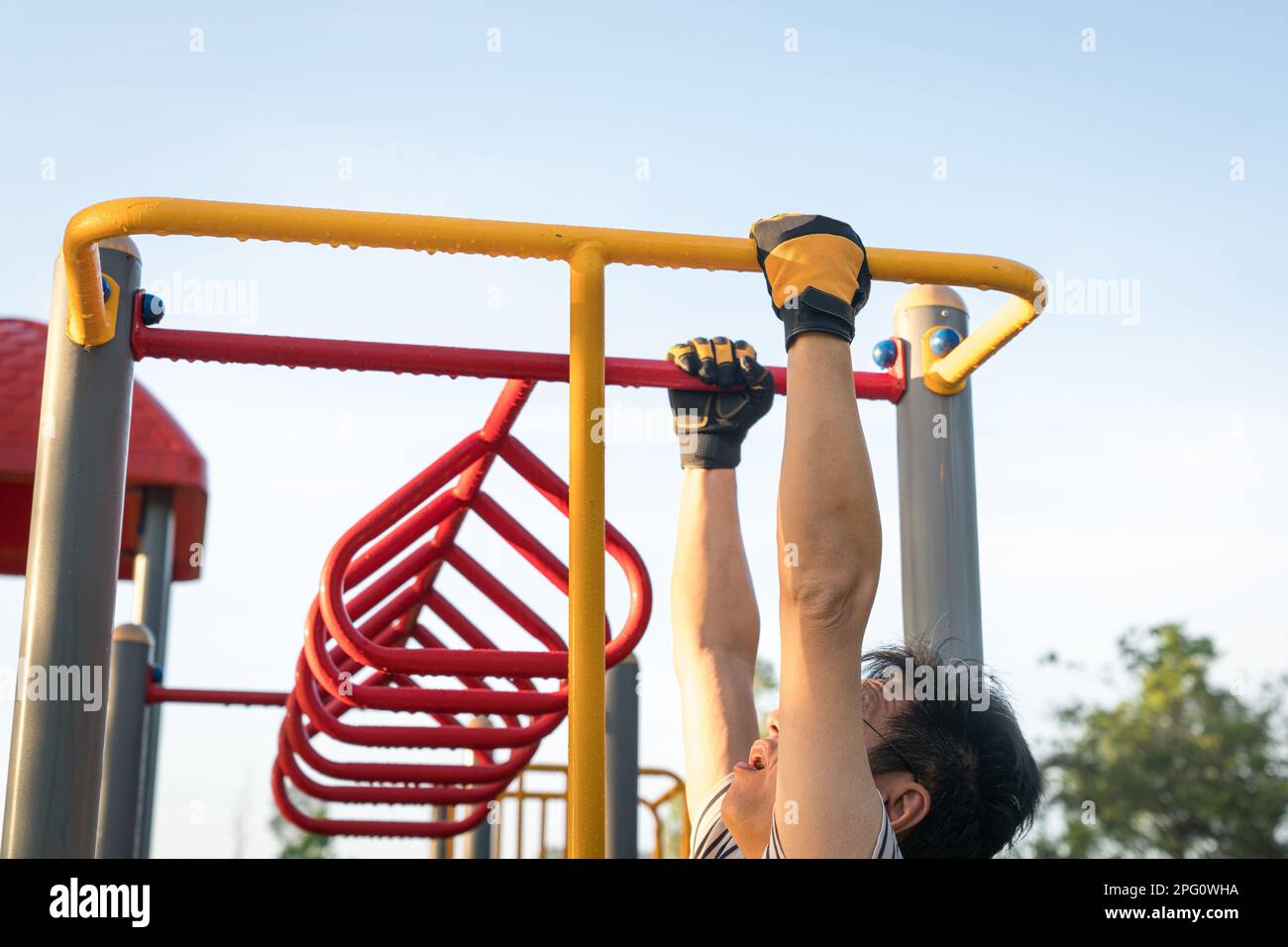 Man working out outdoors, arms swinging on monkey bar. Strength training or fitness exercise concept. Stock Photo