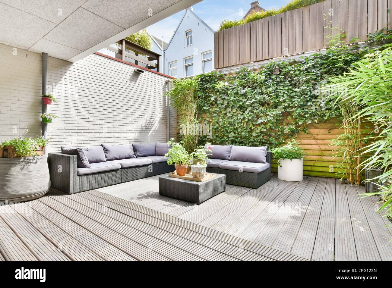 an outdoor living area with wood flooring and plants on the wall, including potted planters and sofas Stock Photo