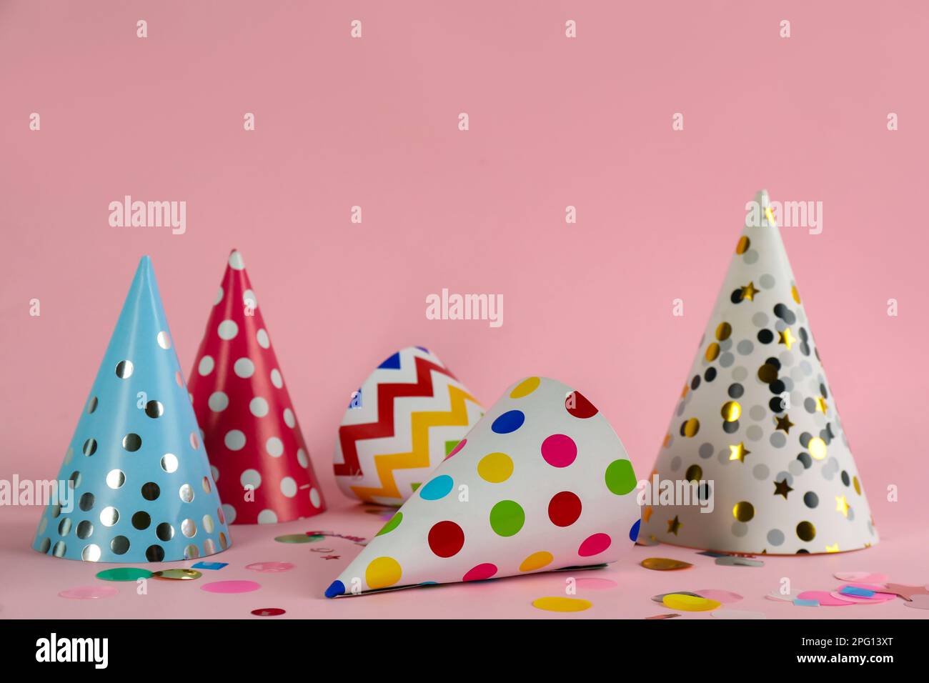 Colorful party hats and confetti on pink background. Space for text ...