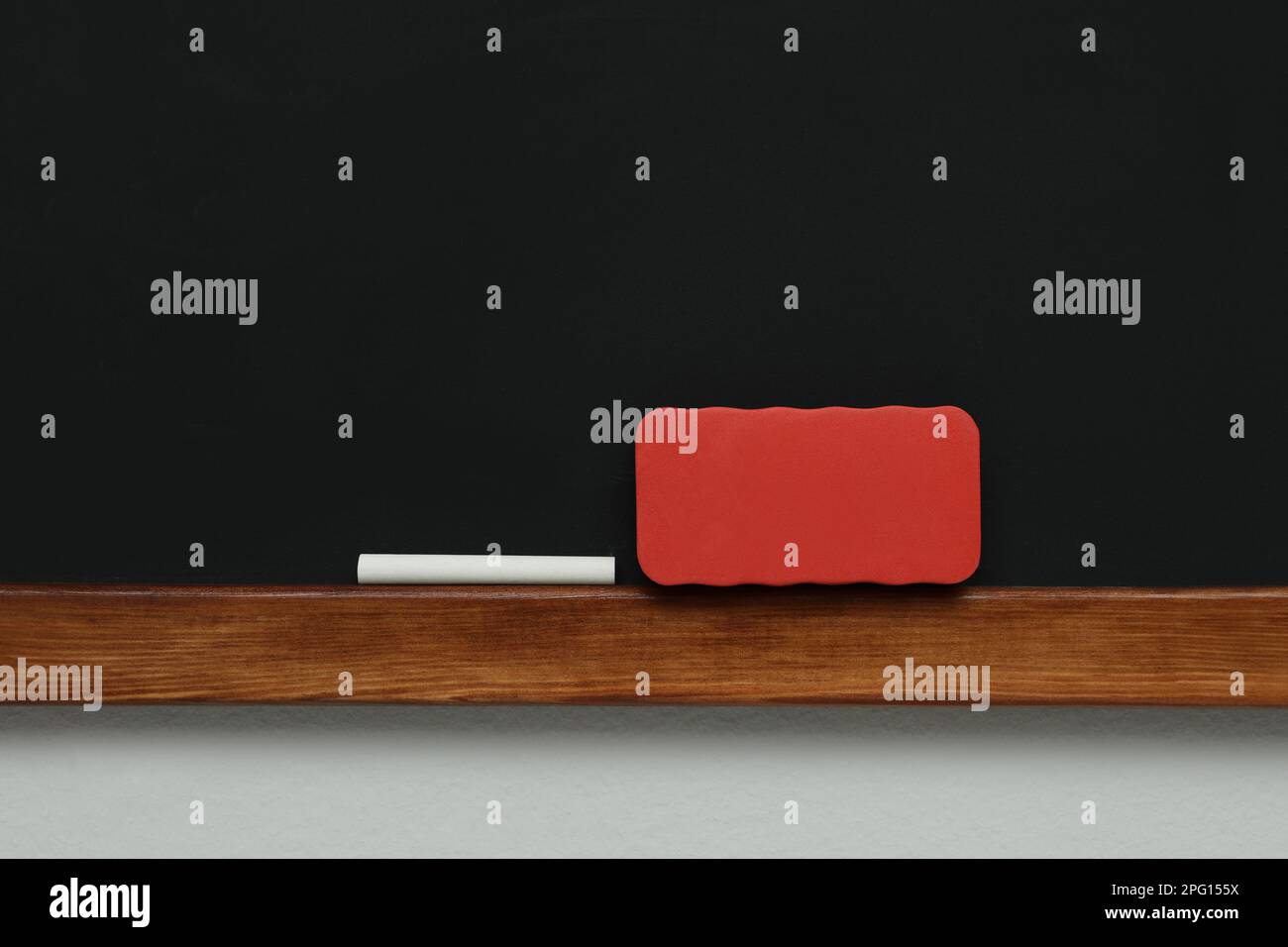 Clean blackboard with chalk and duster hanging on grey wall Stock Photo