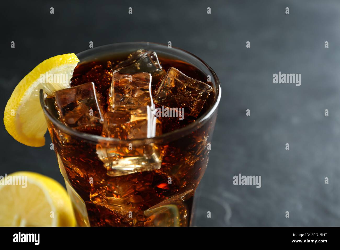 Glass of refreshing soda water with ice cubes and lemon slice on dark ...