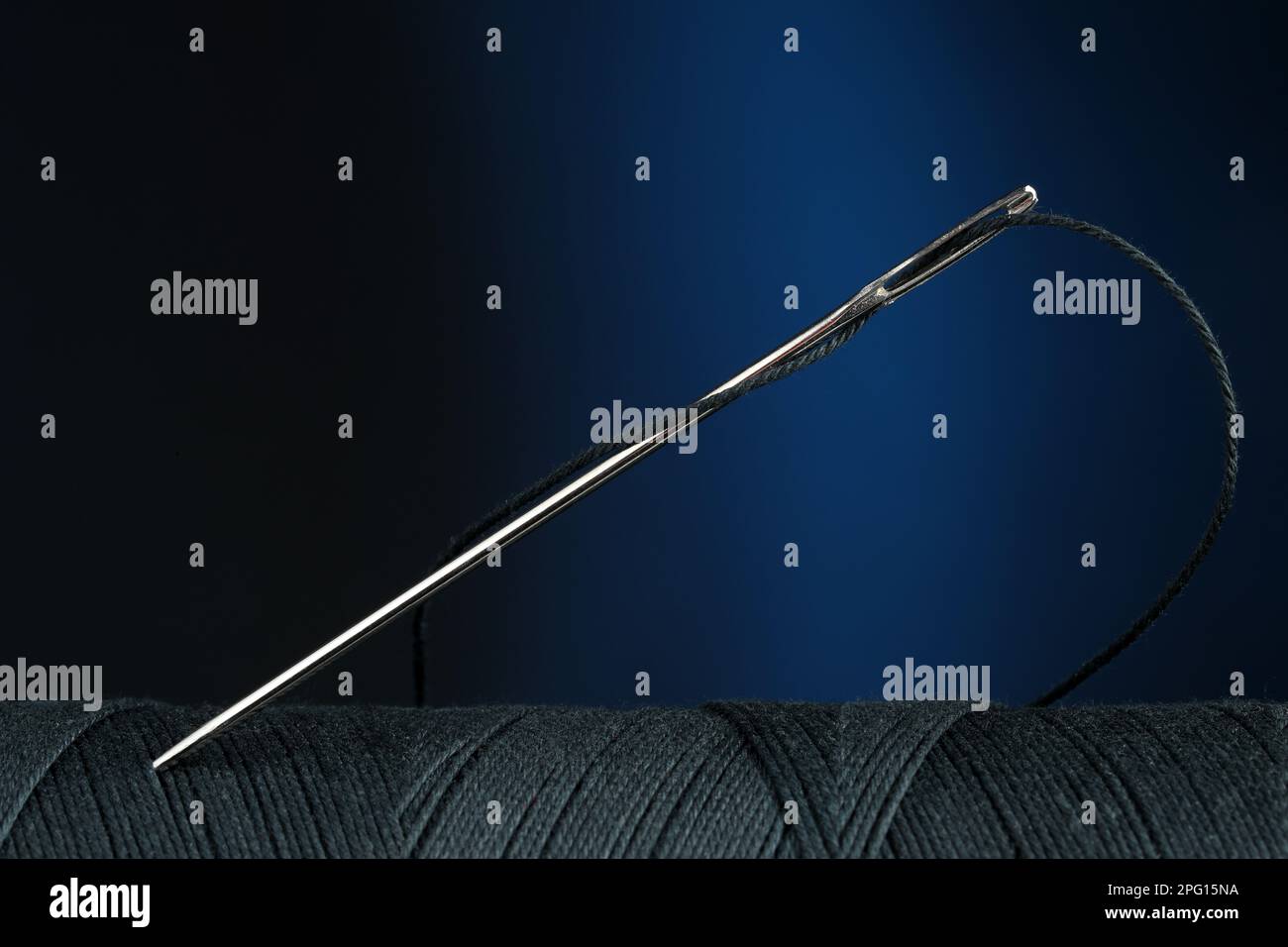 Black sewing thread with needle on dark blue background, closeup Stock Photo