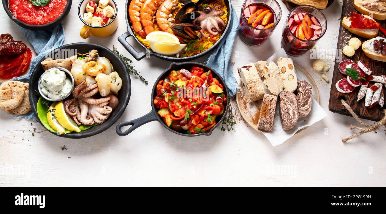 Typical spanish tapas concept. Concept include jamon, chorizo sausage, brushettas, bowl with olives, shrimp, pan with paella, cheese, sangria, churros Stock Photo
